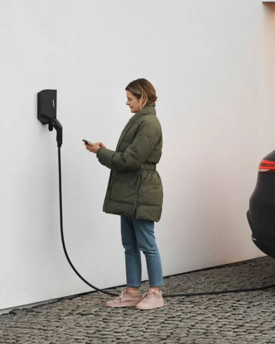 Kvinne lader elbilen med en Easee-lader montert på husveggen